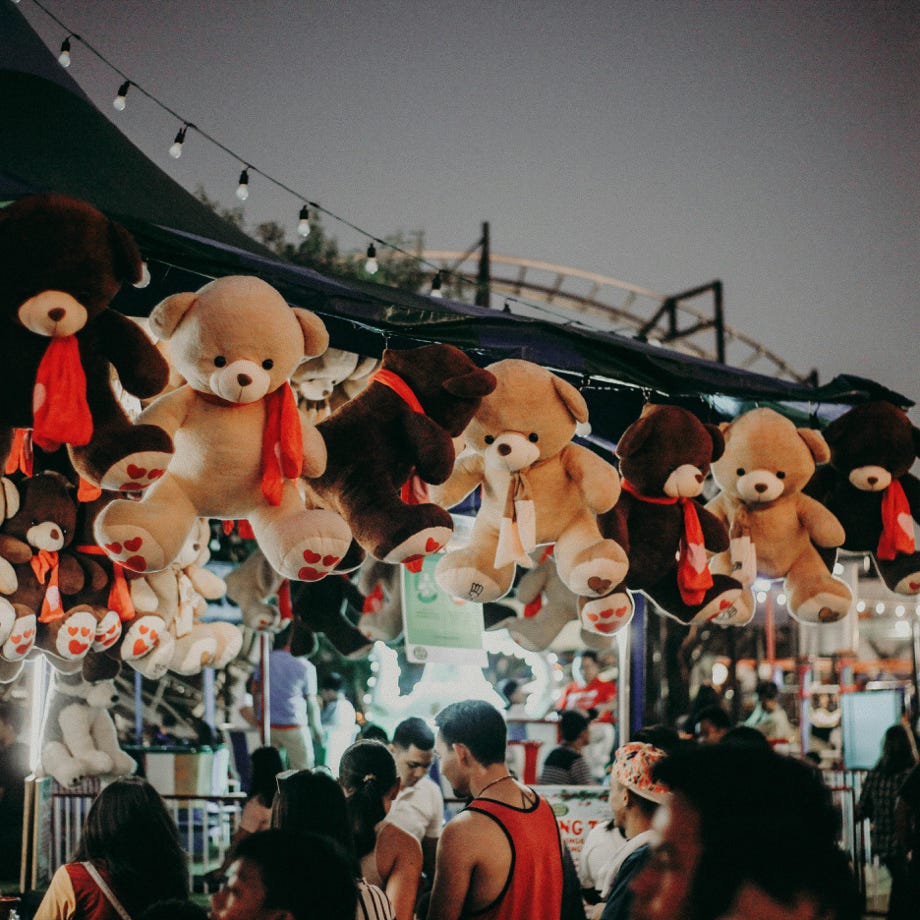 A bustling carnival scene at night featuring teddy bear prizes and a lively crowd.